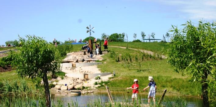 Kinder spielen auf einem begrünten Hügel, der an einem kleinen Fluss liegt